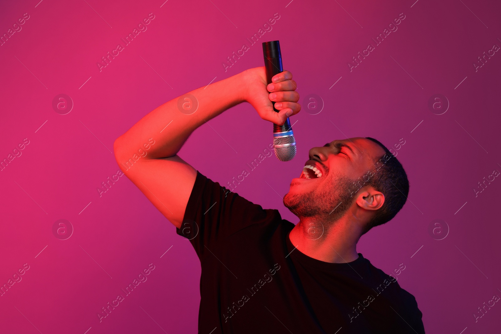 Photo of Handsome man with microphone singing on pink background. Color tone effect