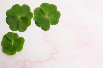 Photo of Beautiful green clover leaves on pink marble table, flat lay. Space for text