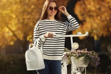 Young woman with stylish backpack and bicycle on autumn day