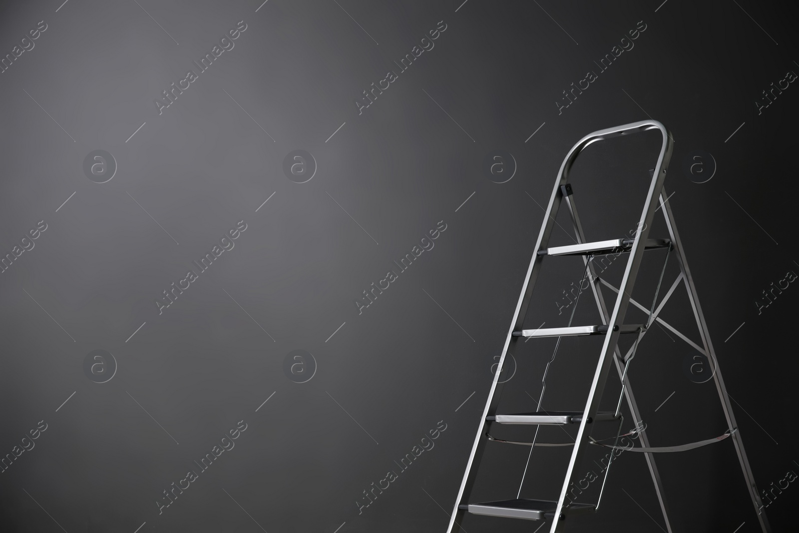 Photo of Modern metal stepladder against grey background. Space for text