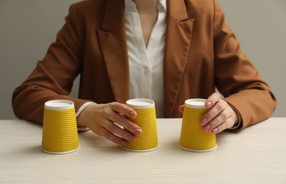Woman playing shell game with yellow cups at white wooden table, closeup