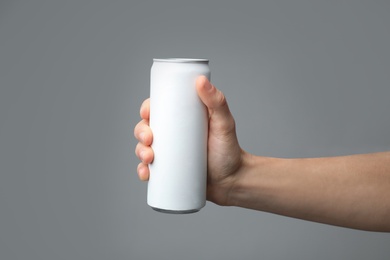 Photo of Man holding aluminum can with beverage on grey background, closeup. Space for design