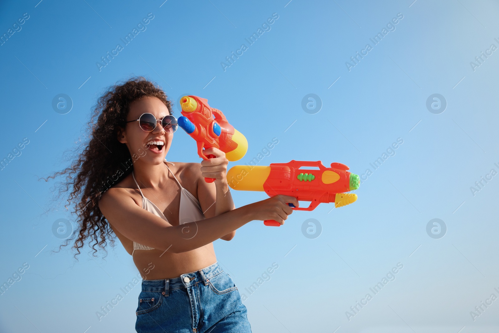 Photo of African American woman with water guns having fun against blue sky