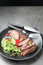 Delicious grilled beef meat served with greens on grey table