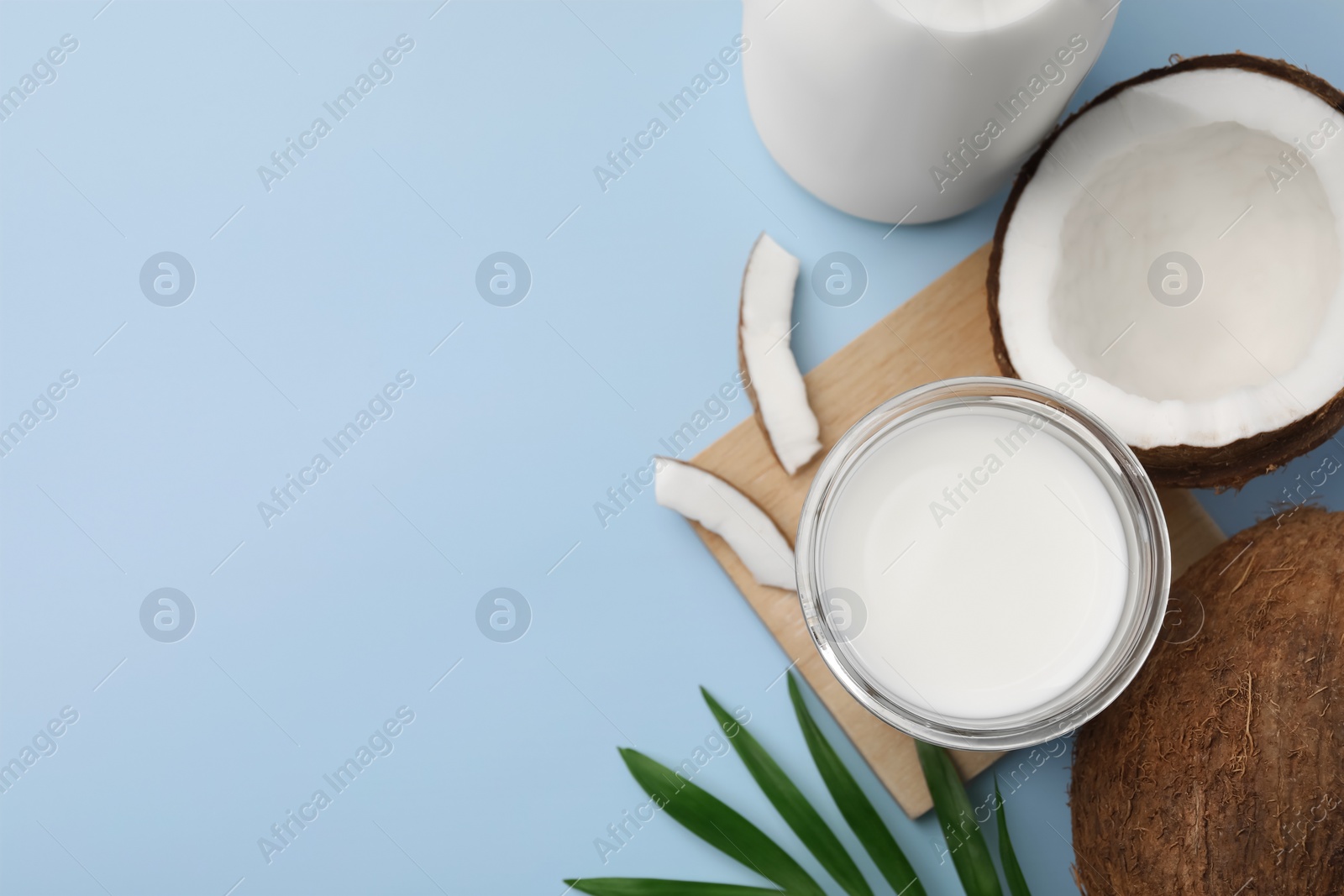 Photo of Glass of delicious vegan milk, coconuts and leaf on light blue background, flat lay. Space for text