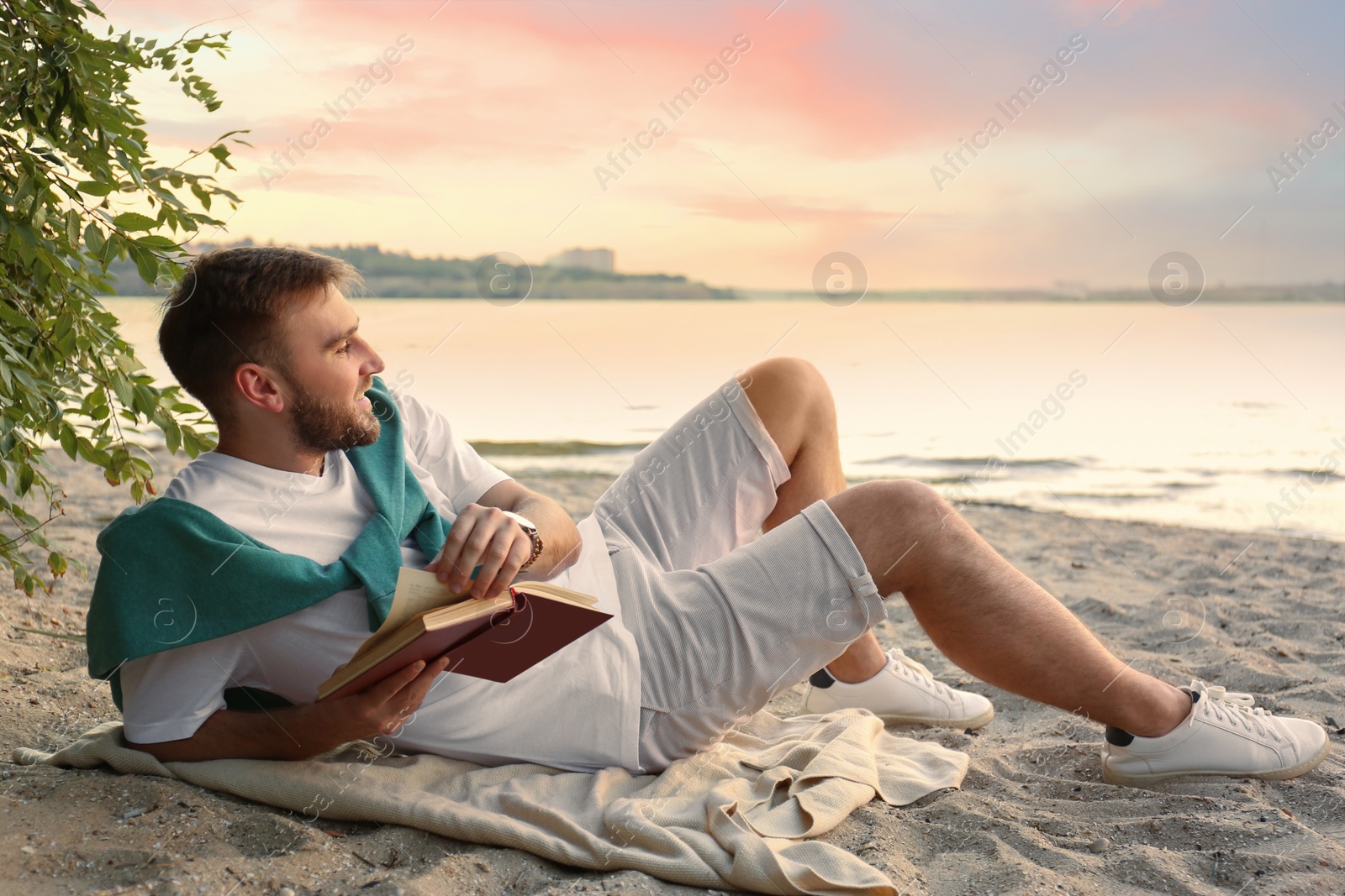 Photo of Young man reading book on sandy beach near sea