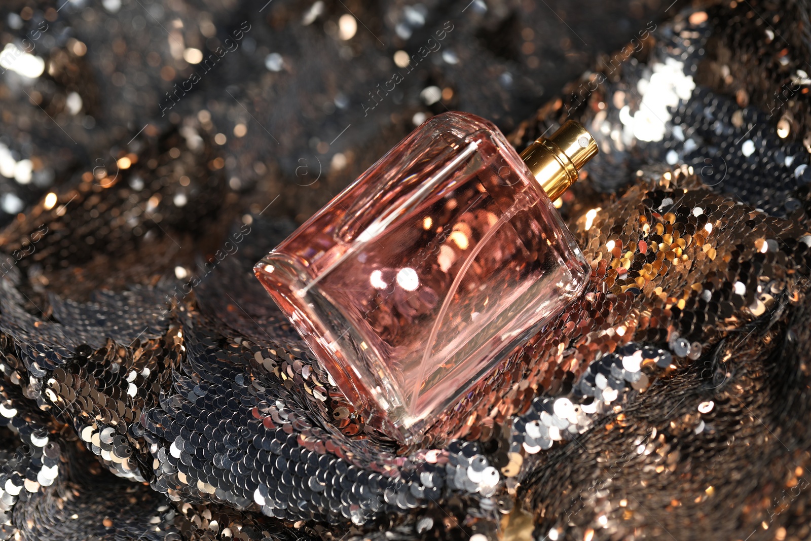 Photo of Luxury perfume in bottle on fabric with shiny sequins, closeup