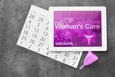 Photo of Flat lay composition with tablet, menstrual cup and calendar on grey background. Gynecological care