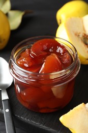 Photo of Quince jam in glass jar, spoon and fresh raw fruits on grey table, closeup