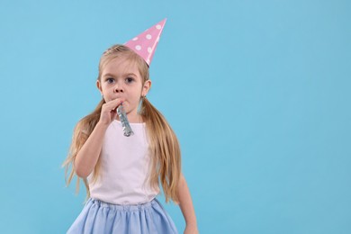 Photo of Birthday celebration. Cute little girl in party hat with blower on light blue background, space for text