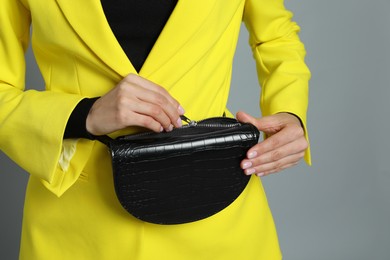 Photo of Young woman with stylish waist bag on grey background, closeup