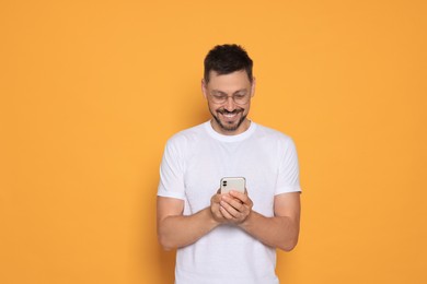 Photo of Happy man with smartphone on orange background