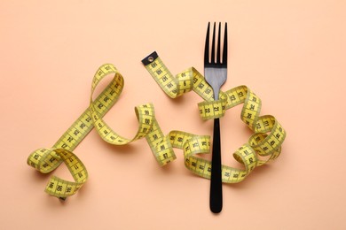 Photo of Measuring tape and fork on pale orange background, top view. Diet concept