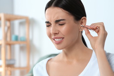 Photo of Young woman cleaning ear with cotton swab at home