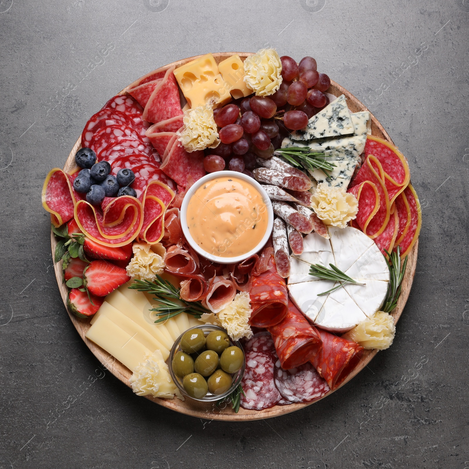 Photo of Wooden plate with different delicious snacks on grey table, top view