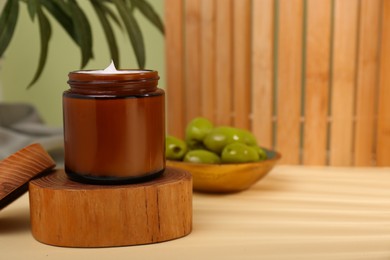 Jar of natural cream with olive essential oil on wooden table, space for text