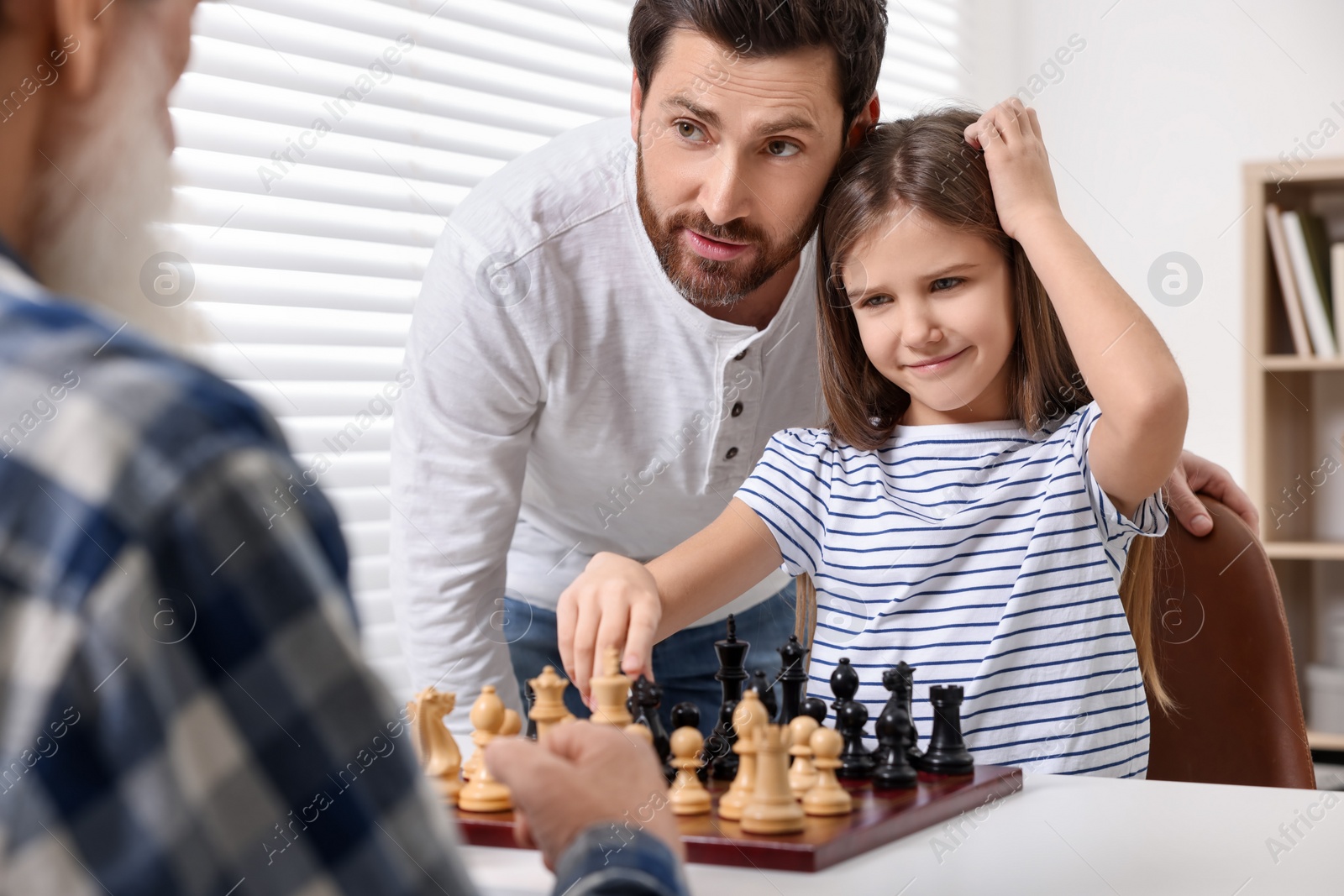 Photo of Family playing chess together at table in room