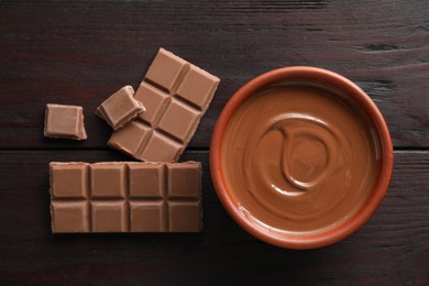 Photo of Tasty milk chocolate paste in bowl and pieces on wooden table, top view