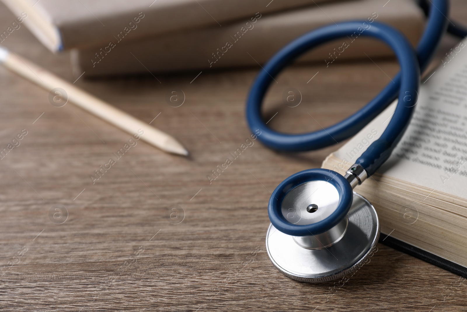 Photo of Student textbook and stethoscope on wooden table, closeup view with space for text . Medical education