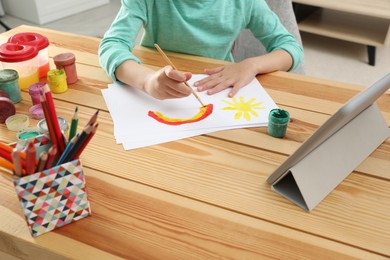 Photo of Little girl drawing on paper with paints at online lesson indoors, closeup. Distance learning