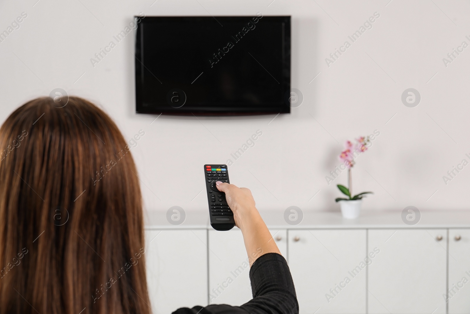 Photo of Woman switching channels on TV set with remote control at home