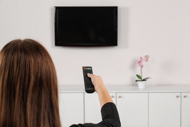 Woman switching channels on TV set with remote control at home