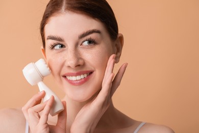 Washing face. Young woman with cleansing brush on beige background, space for text