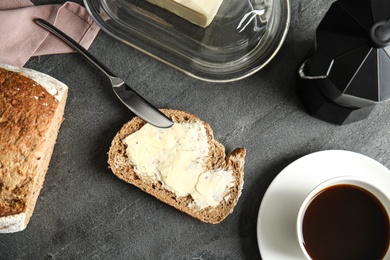 Photo of Tasty bread with butter and coffee served for breakfast on dark table, top view