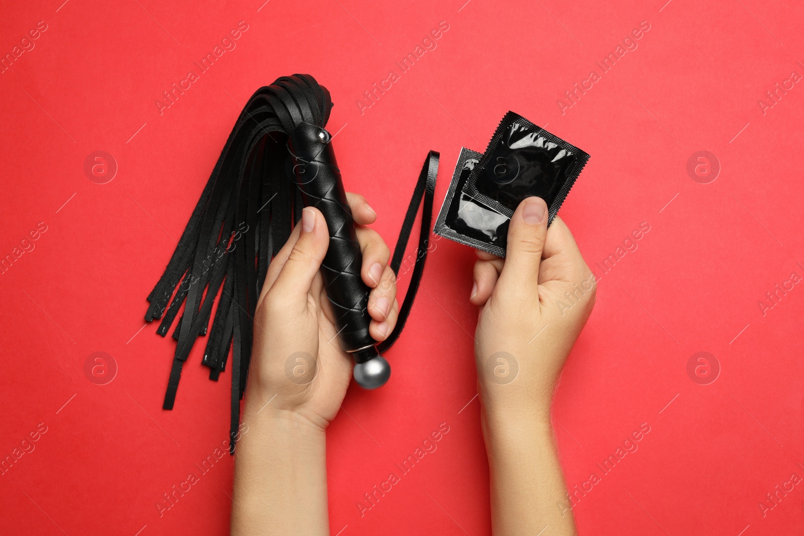 Photo of Woman with whip and condoms on red background, top view. Sex game