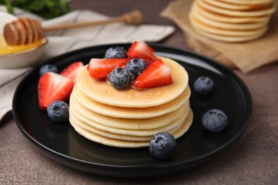 Delicious pancakes with strawberries and blueberries on brown textured table, closeup