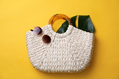 Stylish straw bag and sunglasses on yellow background, flat lay. Summer accessories