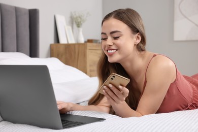 Photo of Happy woman with smartphone and laptop on bed in bedroom
