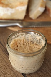 Photo of Sourdough starter in glass jar on wooden table, closeup