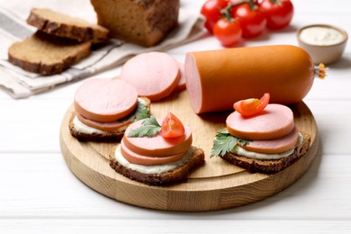 Photo of Delicious sandwiches with boiled sausage, tomato and sauce on white wooden table