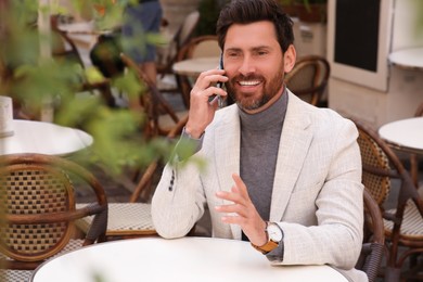 Photo of Handsome man talking on phone at table in outdoor cafe