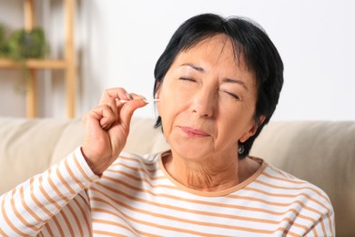 Photo of Senior woman cleaning ear with cotton swab at home