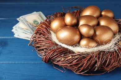 Photo of Golden eggs in nest and dollar banknotes on blue wooden table, closeup. Pension concept