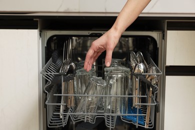 Photo of Woman loading dishwasher with glass and cutlery indoors, closeup