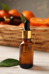 Photo of Bottle of tangerine essential oil and green leaf on white wooden table