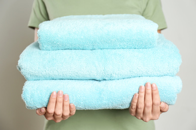Photo of Woman holding stack of fresh towels on grey background, closeup