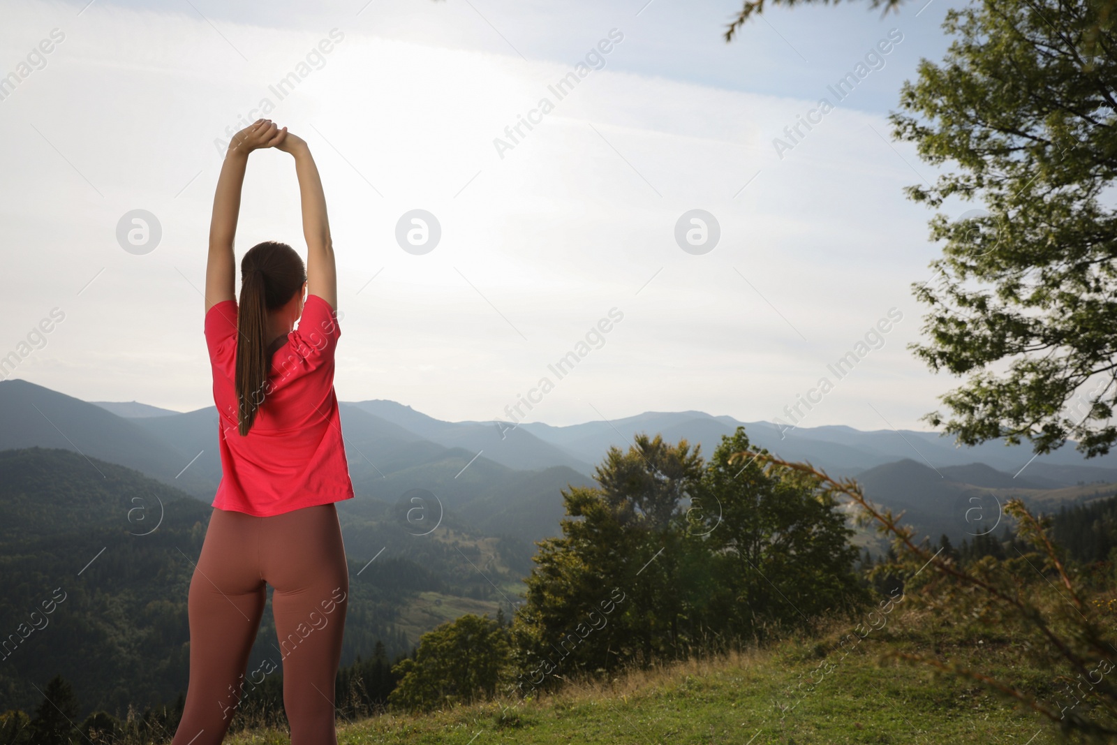 Photo of Woman doing morning exercise in mountains, back view. Space for text