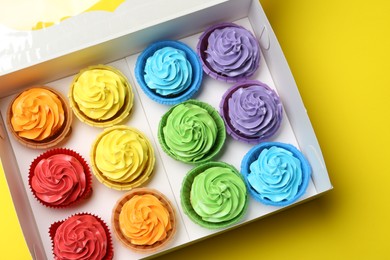 Photo of Tasty cupcakes in box on yellow background, top view