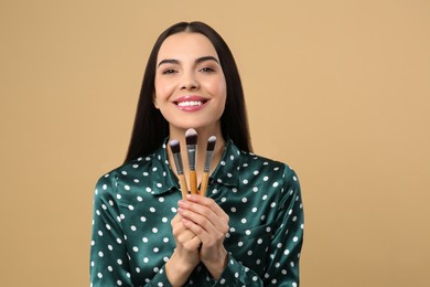 Happy woman with different makeup brushes on light brown background