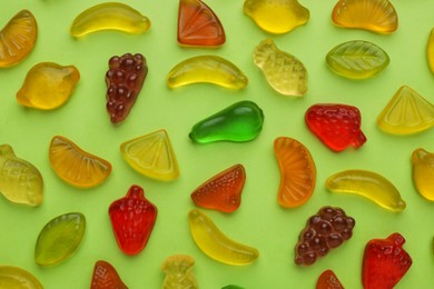 Photo of Tasty jelly candies in shape of different fruits on green background, flat lay