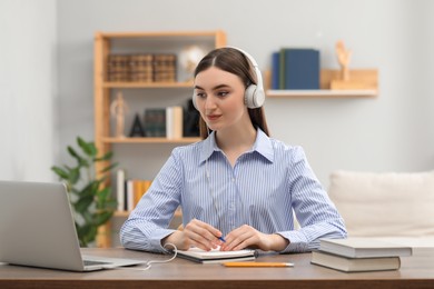 Photo of E-learning. woman taking notes during online lesson at table indoors