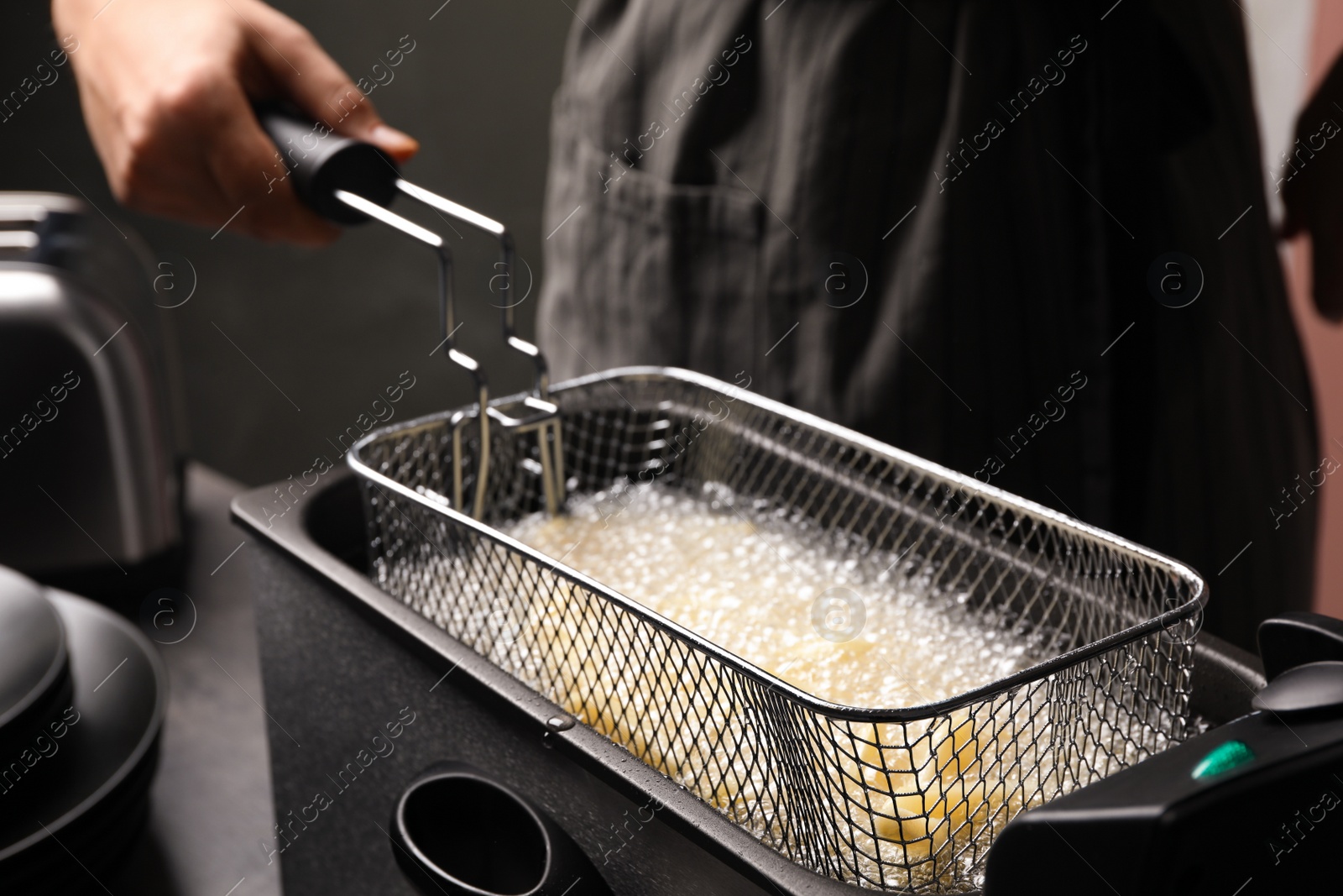 Photo of Chef cooking delicious french fries in hot oil, closeup