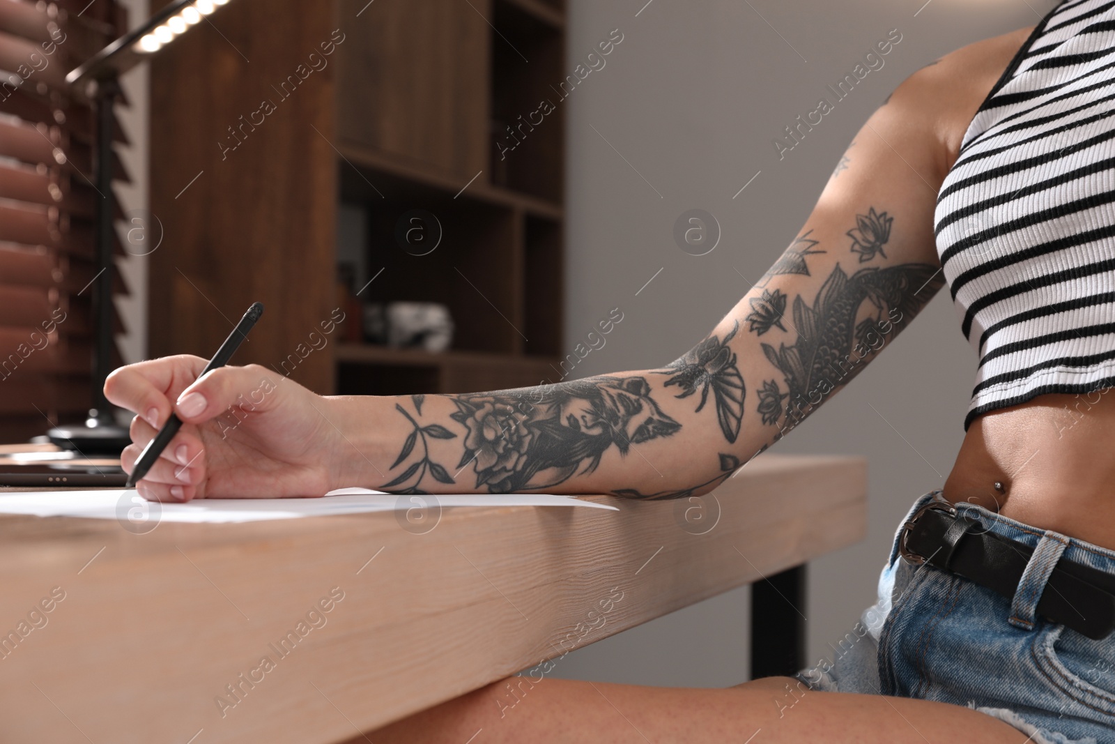 Photo of Woman with tattoos on arm drawing in sketchbook at table, closeup