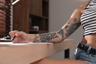 Photo of Woman with tattoos on arm drawing in sketchbook at table, closeup