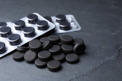 Photo of Activated charcoal pills on black table, closeup. Potent sorbent