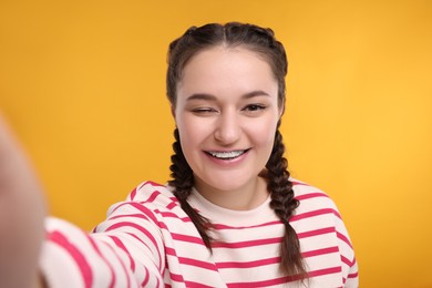 Photo of Smiling woman with braces winking while taking selfie on orange background